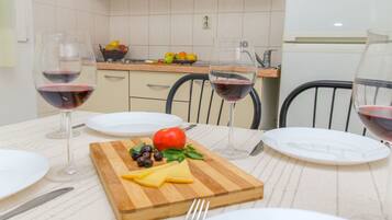 A dining table set with plates, cutlery, and glasses of red wine, with a wooden board holding cheese, tomatoes, and olives.