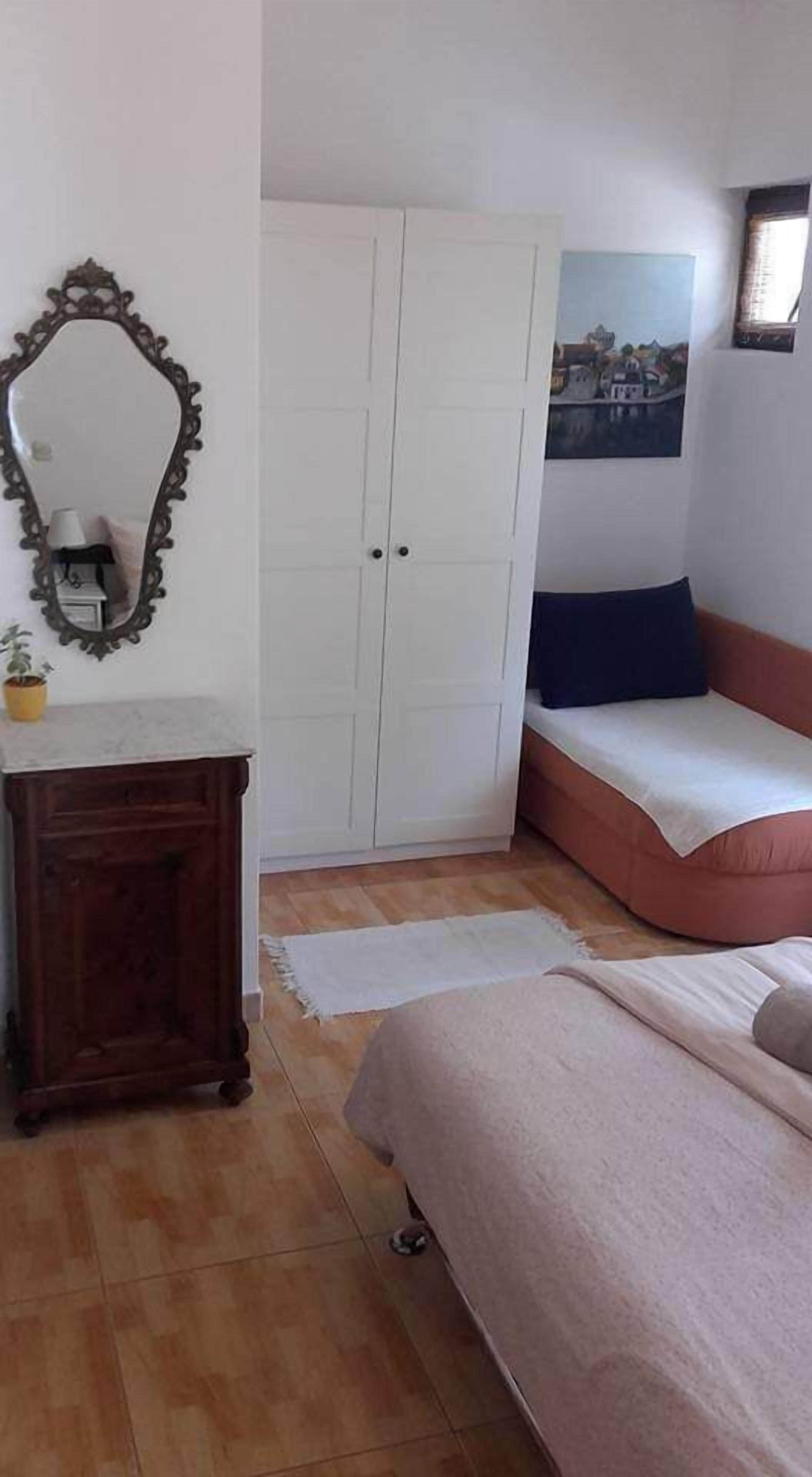 A bedroom with a wardrobe, a bed, a bedside table, a mirror, and a painting on the wall.