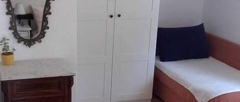 A bedroom with a wardrobe, a bed, a bedside table, a mirror, and a painting on the wall.