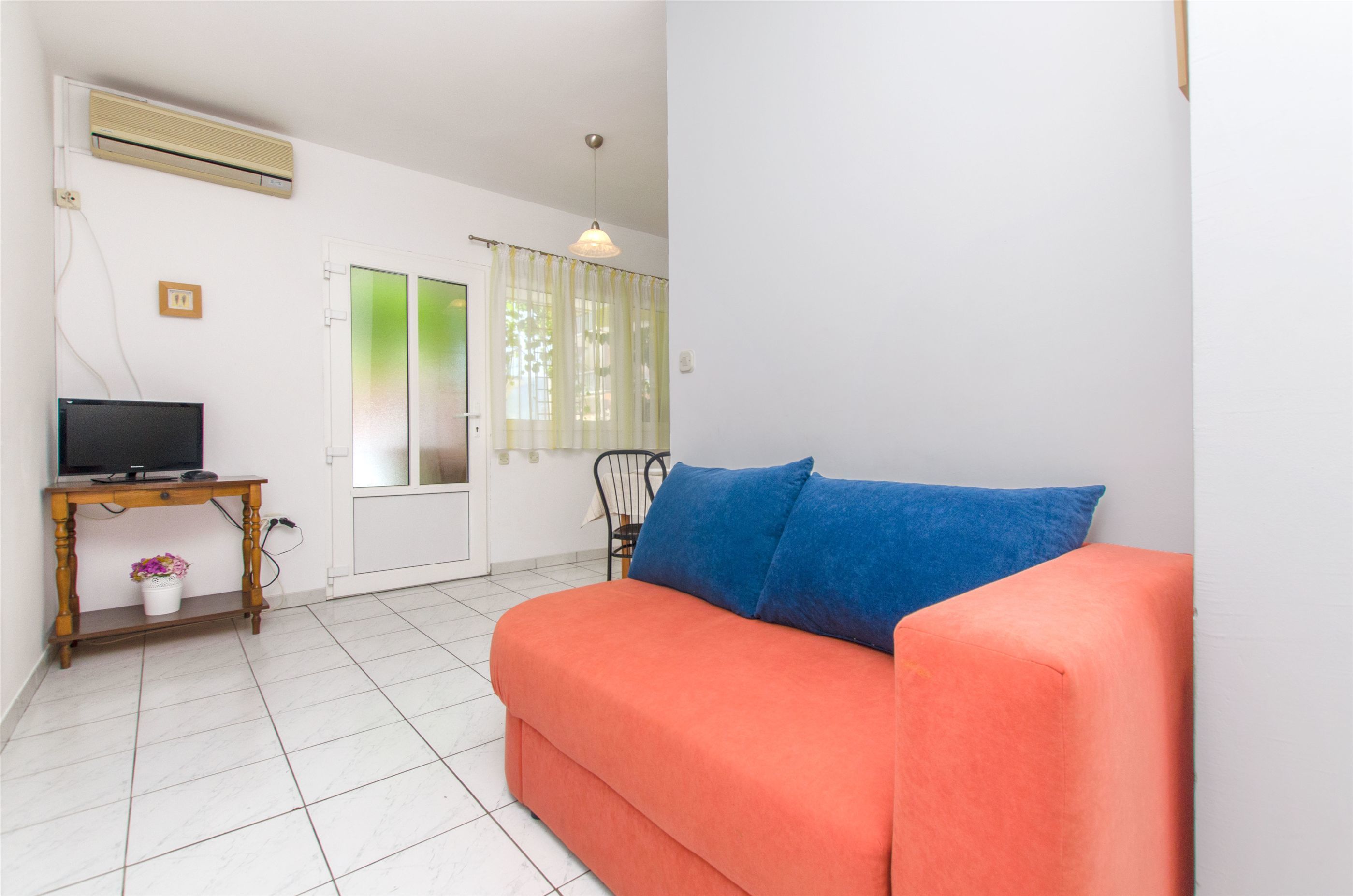A living room with a sofa, a television on a wooden table, and a window with curtains.