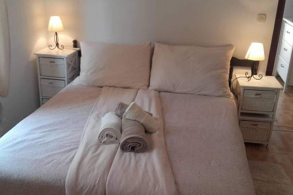 Una cama bien hecha con toallas enrolladas, dos mesitas de noche con lámparas y una ventana con cortinas.