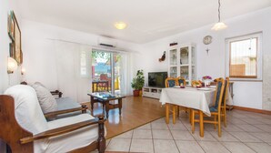 A living room with a sofa, dining table, chairs, a TV, and a window. - Apartments Anita (Vrboska)