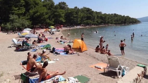A beach with people sunbathing, swimming, and a tent set up. - Apartments Anita (Vrboska)