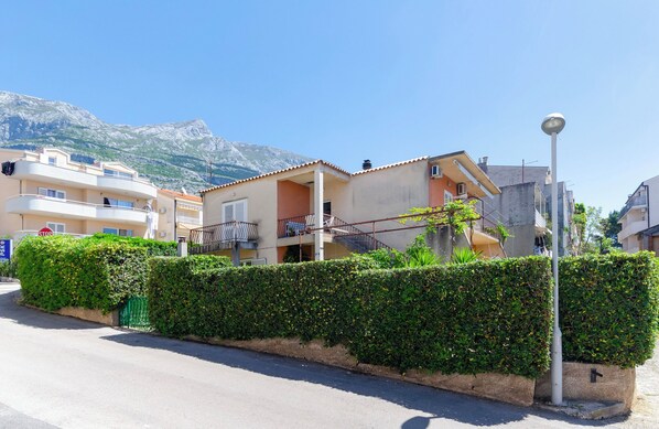 A residential building with balconies, a street lamp, and a mountain in the background. - Apartments Katica (Makarska)