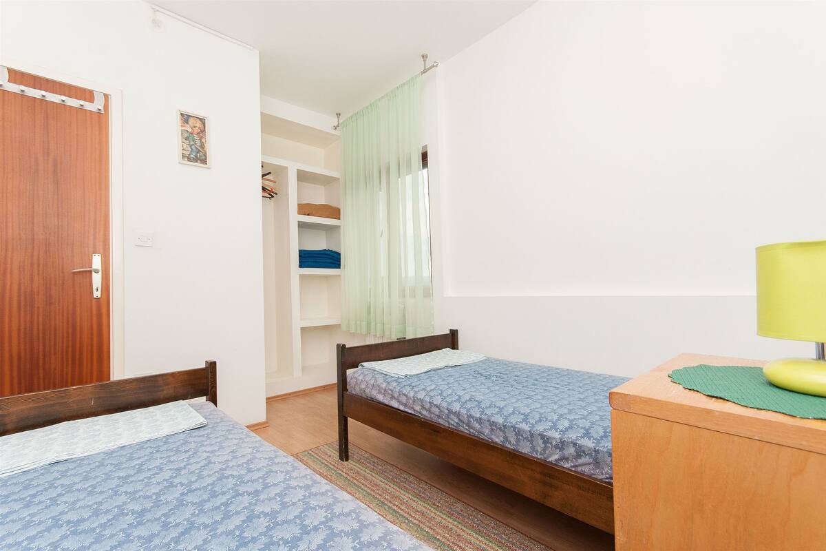 A bedroom with two wooden beds, a wardrobe, a closet, and a bedside table with a lamp.