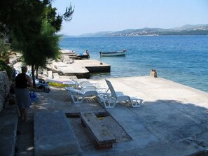 A waterfront area with a concrete pier, lounge chairs, and a small boat.