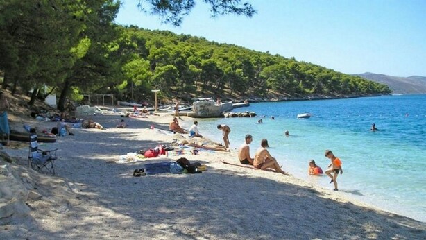 A beach with people sunbathing and swimming, surrounded by trees and boats. - Apartments Marko (Okrug Donji)