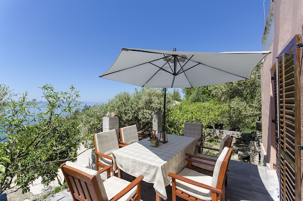 A patio with a table and chairs, an umbrella, and a view of the sea. - House Miroslav (Podgora)