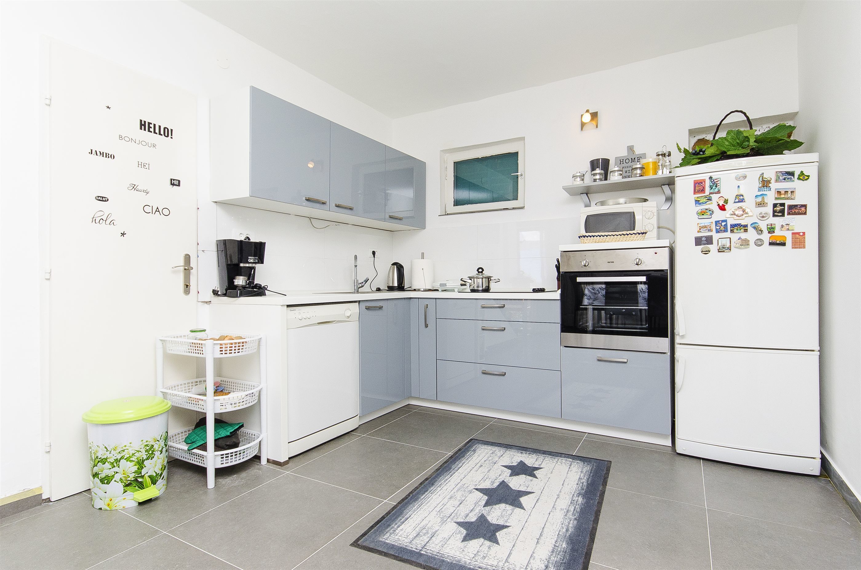 A compact kitchen with white cabinets, a microwave, a stove, and a refrigerator adorned with magnets.