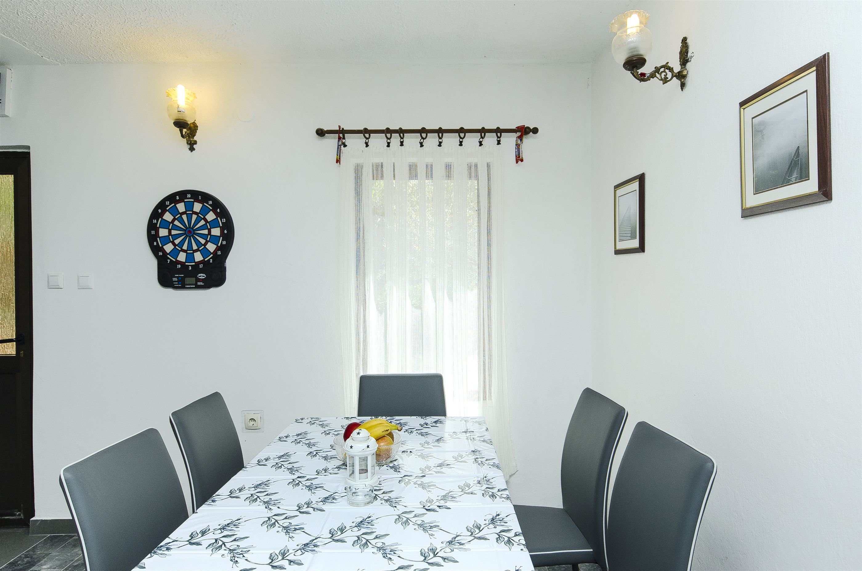 A dining area with a table set for four, a dartboard, and two wall-mounted lights.