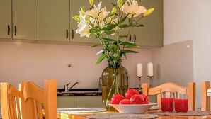 Eine Küche mit Esstisch, Stühlen, einer Vase mit Blumen, einer Fruchtschale und zwei Kerzen.