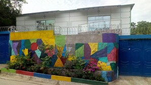 A building with a colorful geometric mural, a gated entrance, and a small garden area with flowering plants. - El tucan es un lugar maravilloso dónde descansas comodamente (Bonda)