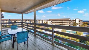 A covered outdoor area with a table and chairs, overlooking a pool and buildings. - Lighthouse Point Condo Unit 2C (Tybee Island)