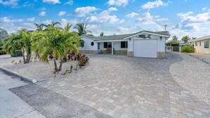A single-story house with a garage, a paved driveway, and a small garden with palm trees. - AUGUST Opening, Fishermen, Couples, Families, Pool, Cabana Club (Key Colony Beach)