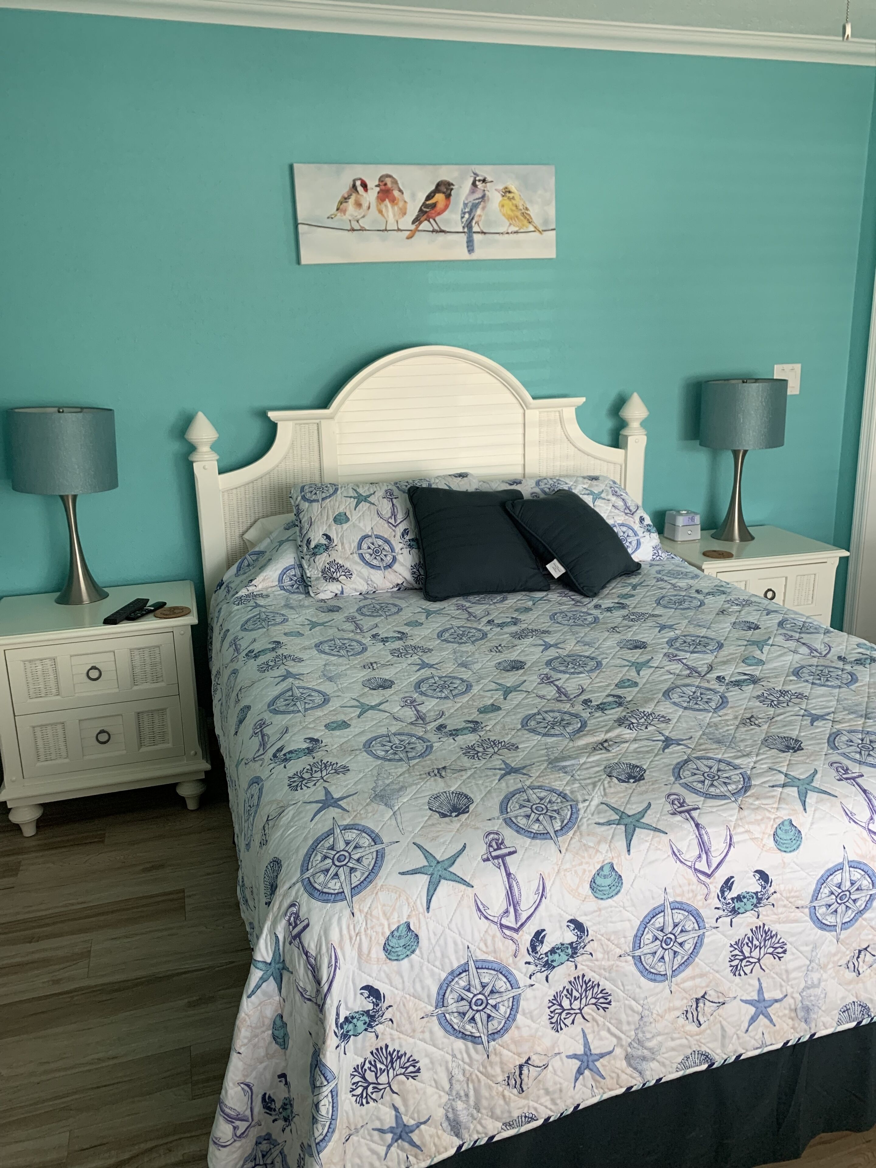 A bedroom with a bed, two nightstands, a wall painting, and a teal wall.