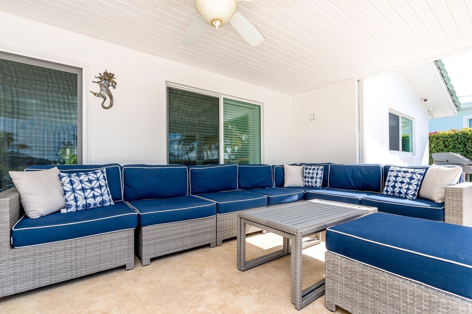 A covered outdoor seating area with a large sectional sofa, a small table, and a ceiling fan.