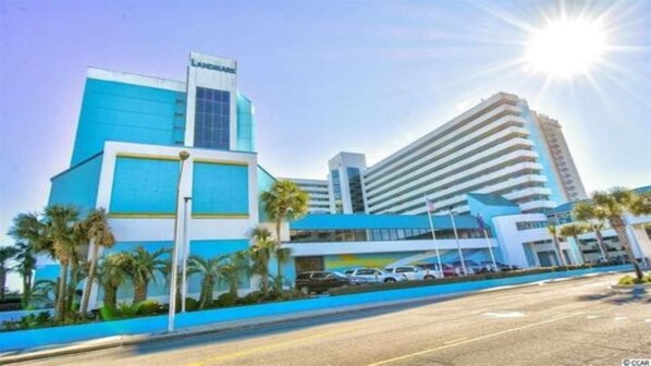 A modern hotel with a prominent blue and white facade, a visible name sign, and a parking area with several cars. - Lee's Myrtle Beach Condo (Myrtle Beach)