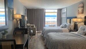 Hotellihuone, jossa on kaksi sänkyä, työpöytä tuolilla, televisio ja ikkuna, jossa on verhot.