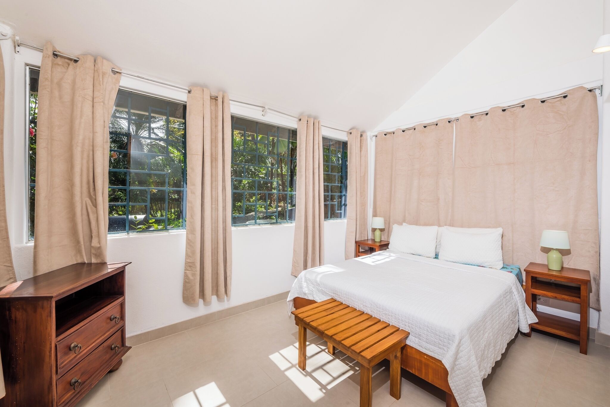 A bedroom with a bed, wooden nightstands, a wooden bench, and a dresser.
