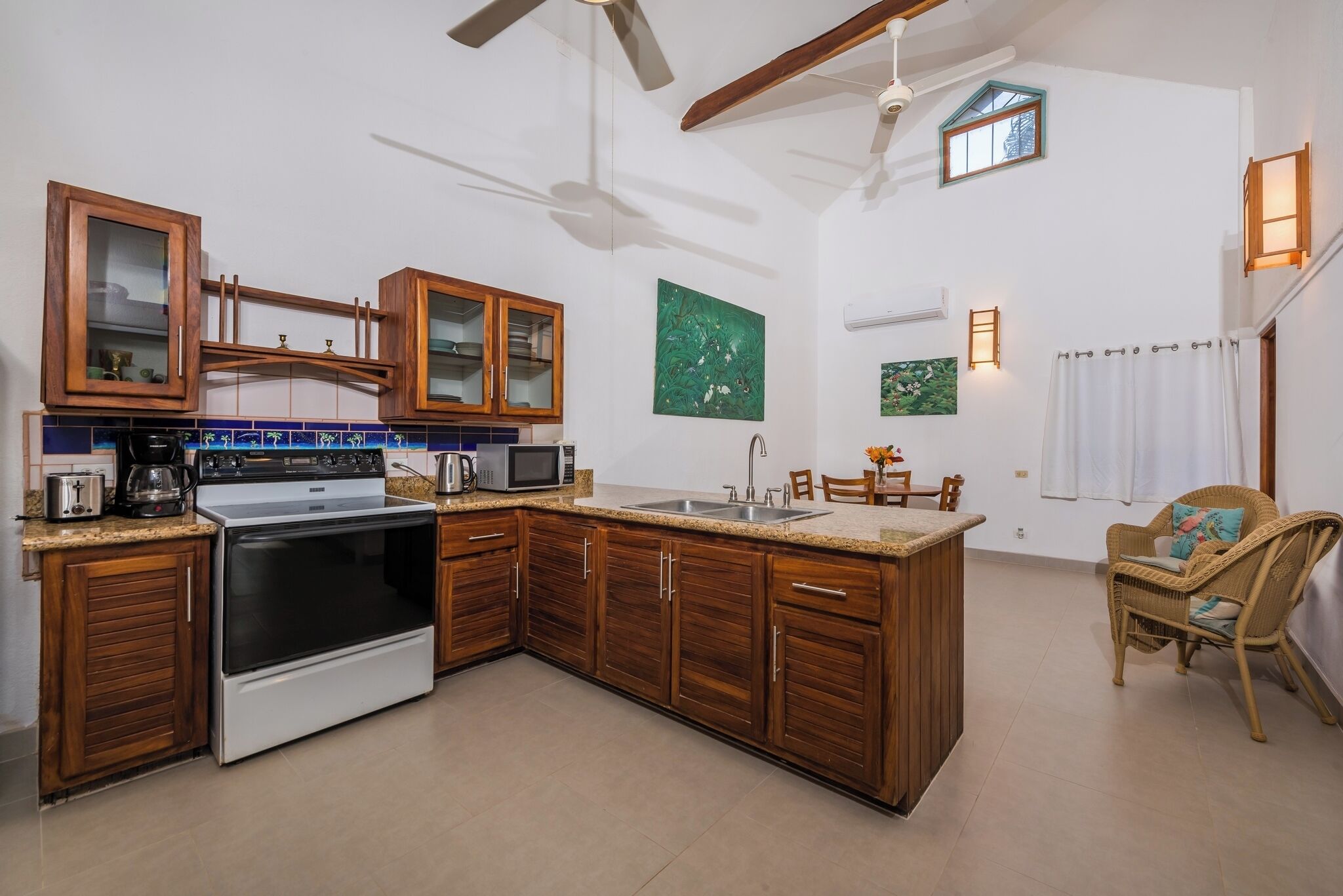 Une cuisine avec des meubles de rangement en bois, une cuisinière, un four à micro-ondes et un évier. On y trouve deux chaises et une table sur laquelle est posé un vase de fleurs.