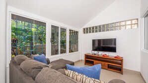 Un salon avec une grande fenêtre, un téléviseur posé sur un meuble en bois et un canapé agrémenté de coussins.