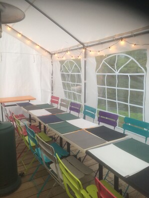 A tented room with tables and chairs, large windows, and string lights. - Camping des Nières (Ebreuil)
