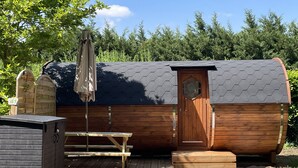 Una cabaña de madera con una puerta hexagonal, una mesa de picnic y un banco cubierto.