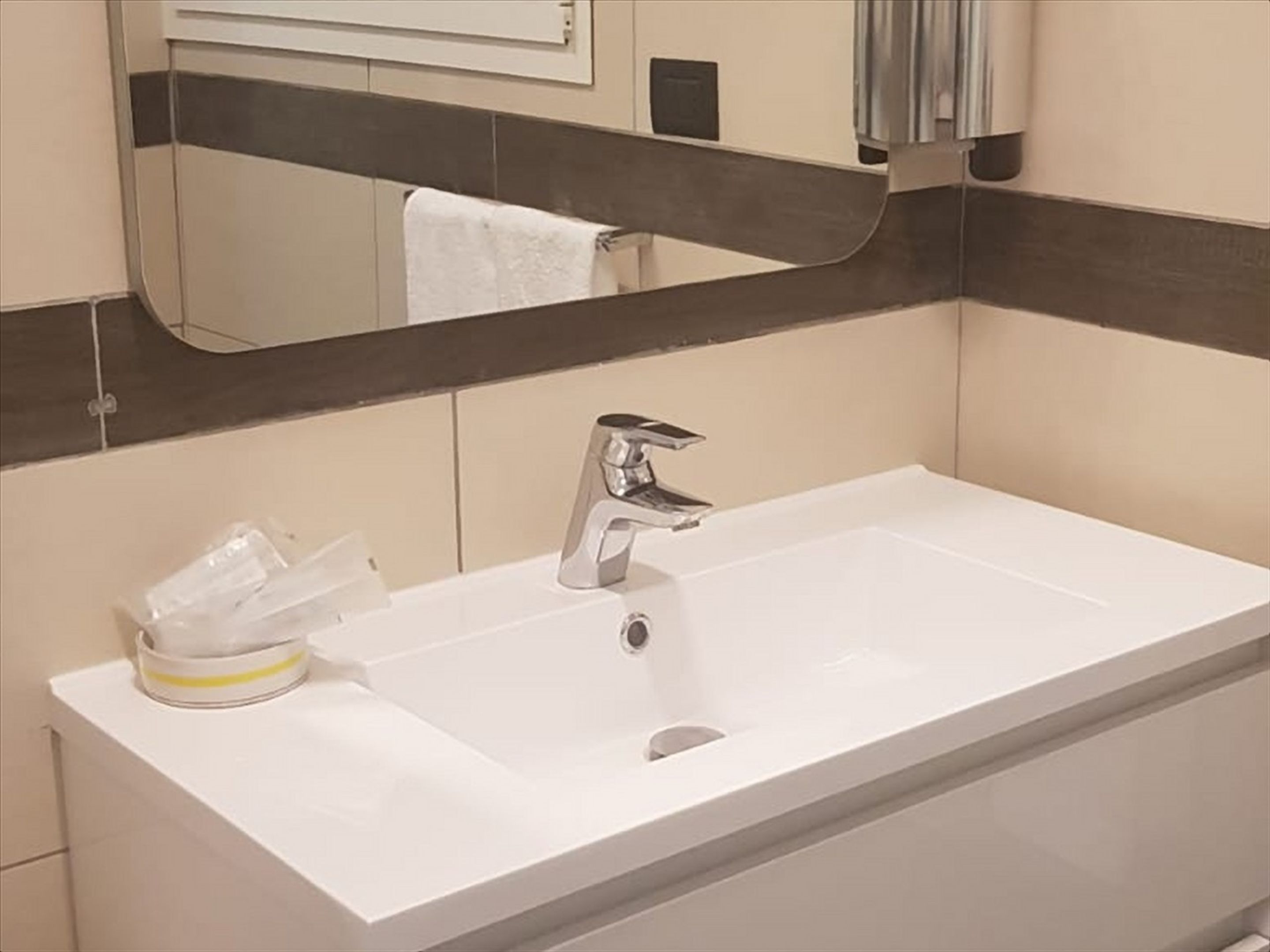 Un baño con un lavamanos blanco, un espejo y una toalla colgada en la pared.