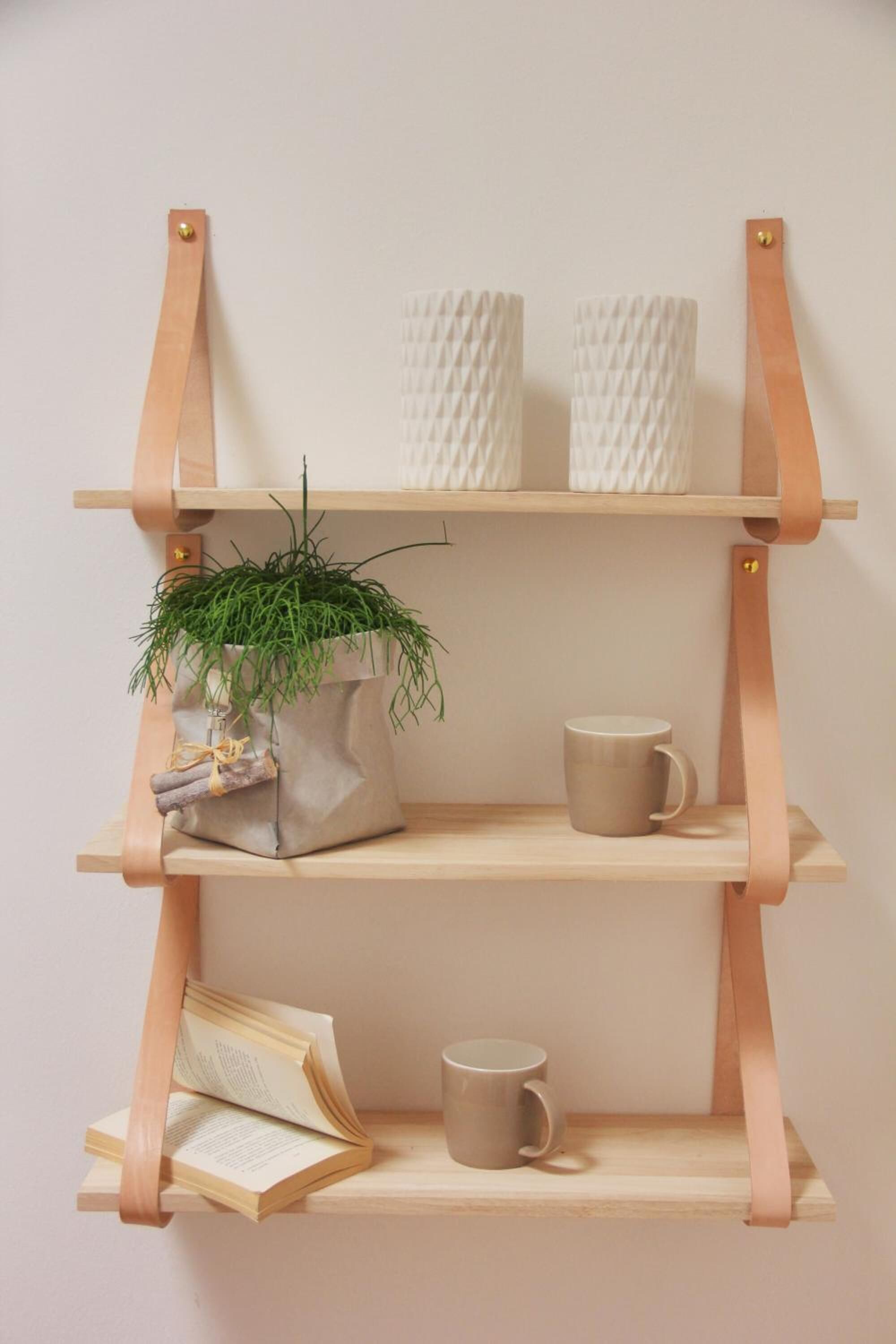 A wooden shelf with two white textured vases, a potted plant, a mug, and an open book.