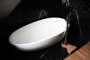Un baño moderno con un lavamanos ovalado blanco, paredes de azulejos negros y un mueble de tocador de madera.