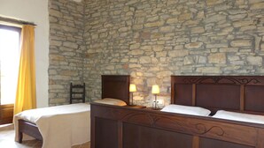 Un dormitorio con dos camas de madera, paredes de piedra, una silla y una mesita de noche con lámparas.