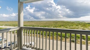 A balcony with a view of a grassy landscape and a cloudy sky. - Relax by the Waves | Beachside Condo with Pool & Ocean Views (Corpus Christi)