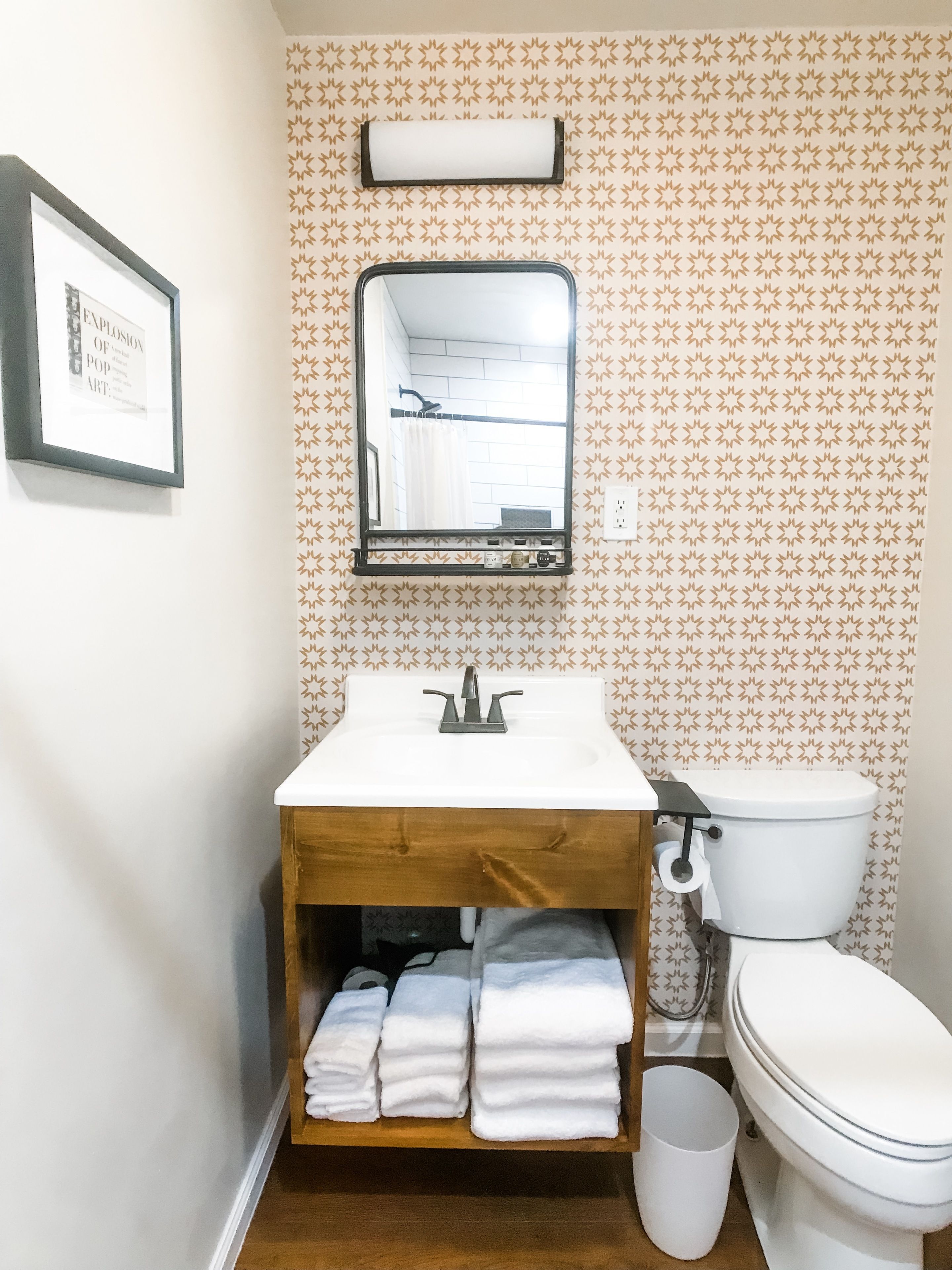 Une salle de bain avec un meuble-lavabo en bois, un évier, un miroir, des toilettes et un luminaire fixé au mur.