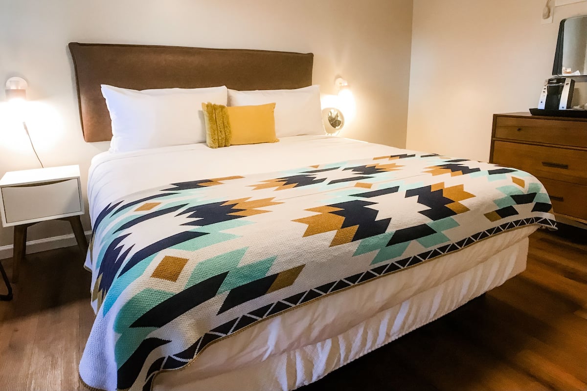 A neatly made bed with a patterned blanket, a wooden headboard, and bedside lamps.