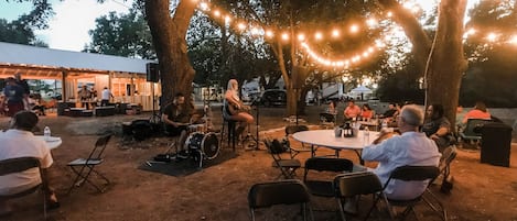 Un espacio al aire libre con mesas y sillas, rodeado de árboles y luces colgantes.