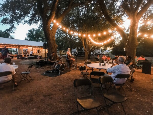 An outdoor seating area with tables and chairs, surrounded by trees and string lights.