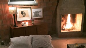 Ein Schlafzimmer mit Kamin aus Ziegelsteinen, einem Bett, einem Nachttisch mit Lampe und gerahmten Bildern an der Wand.