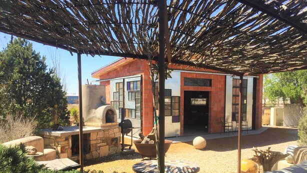 Eine rustikale Außenpatio mit einem Kamin aus Stein, einer Holzpergola und einem Backsteinhaus im Hintergrund.