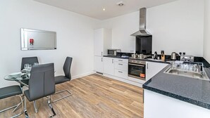 A modern kitchen with white cabinets, a stainless steel range hood, a microwave, and a sink. - City Suites by Guestz (Chester)