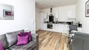 A modern kitchen with white cabinets, a stainless steel range hood, and a dining area with a glass table and chairs.