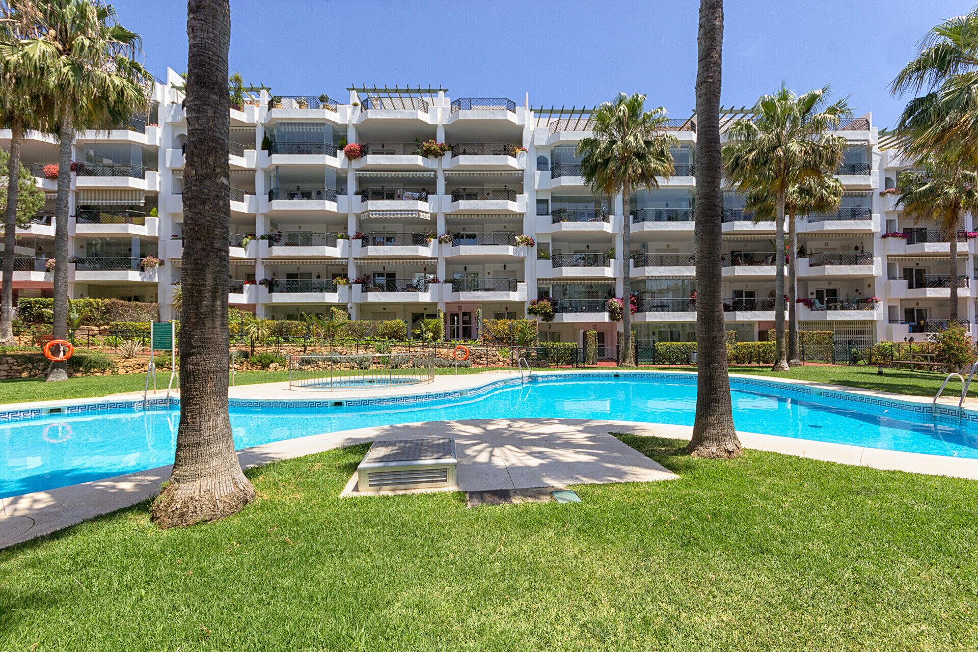 Un hôtel à plusieurs étages doté d’une piscine entourée de palmiers et de pelouses bien entretenues.
