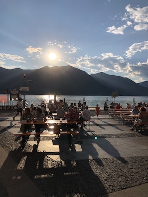 A lakeside terrace with tables and chairs, overlooking a body of water and mountains.