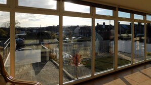 A spacious room with large windows offering a view of a residential area. - Sky View -  Enjoy panoramic roof top views from the sunny conservatory or outside deck. (Sheringham)