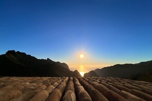 Un paisaje con el sol poniéndose tras montañas y una serie de estructuras cilíndricas al frente.