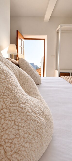 A bedroom with a large bed, a bedside lamp, and a view of the outdoors.