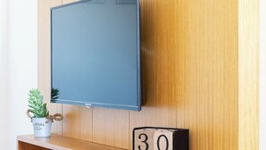 En väggpanel av trä med en väggmonterad platt-TV, en liten krukväxt, en trähylla och en digital klocka som visar "30 MAJ".