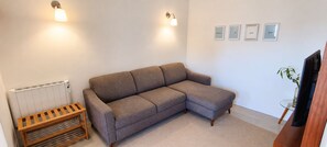 Una sala de estar con un sofá seccional gris, un banco de madera, un radiador y una pared con cuadros enmarcados.