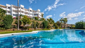 A swimming pool with a view of a multi-story building with balconies, surrounded by greenery and palm trees. - I02 El Alarife - Apartment with sea views (Sitio de Calahonda)