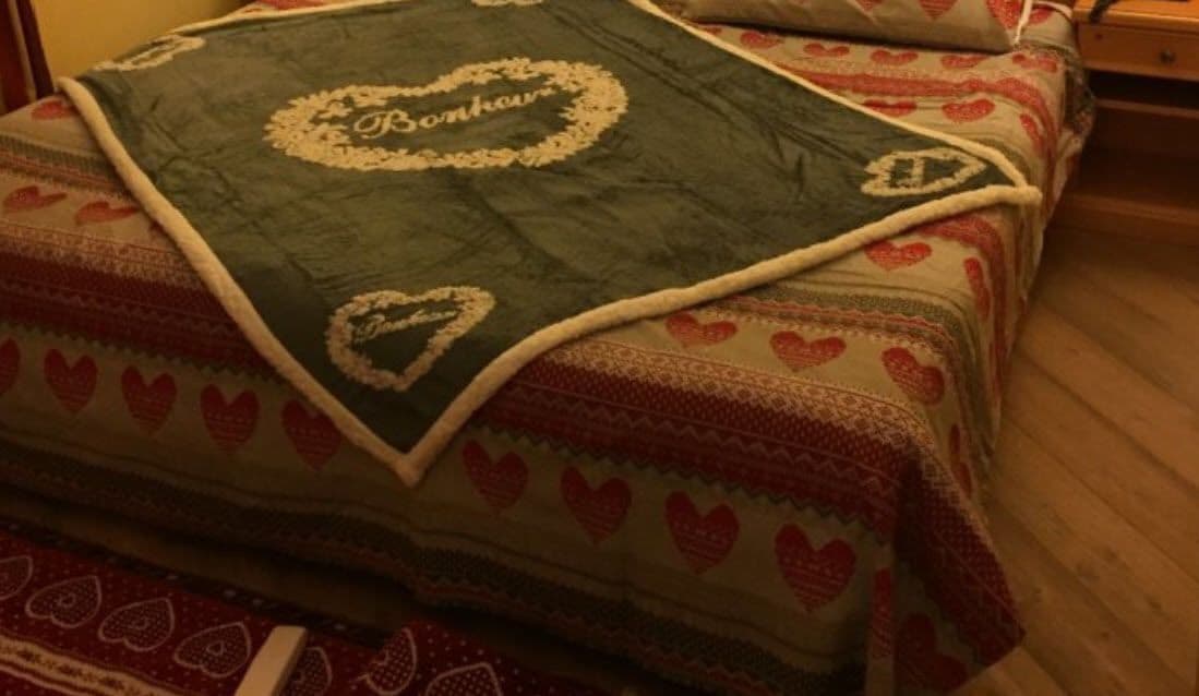 Cama com colcha estampada em padrão de coração e manta bordada com um nome.