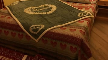 A bed with a heart-patterned bedspread and a blanket with a name embroidered on it.